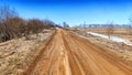 A dry dirt clay rural road in a field, stretching to the horizon in early spring. Rustic landscape