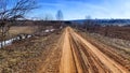 A dry dirt clay rural road in a field, stretching to the horizon in early spring. Rustic landscape