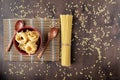 Dry fettuccine pasta in a deep red bowl on a bamboo napkin with wooden spoons around the edges and spaghetti on a wooden