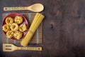 Dry fettuccine pasta in a red ceramic Cup on a softly blurred background of patterned kitchen utensils and bamboo napkins and dark