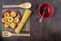 Dry fettuccine pasta on a red ceramic plate on a softly blurred background of patterned kitchen utensils and bamboo napkins and