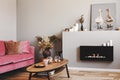 Dry flowers in pottery vase on small wooden table next to velvet pink couch in grey living room