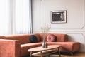 Flowers in stylish dark vase on wooden coffee table in front of ginger colored corner sofa