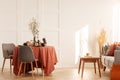 Flowers in vase on dining table covered with dark orange tablecloth