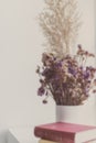 Dry flowers in white jar with books on table close to window with copy space. Minimal and simple stylish fo decoration for living