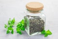 Dry herbal mint tea in a glass jar with fresh peppermint on background