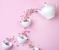 Dry herbal tea is a tea rose poured from a white porcelain teapot into a cup on a pink surface