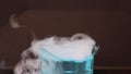 Dry ice in a glass of blue water and engender white smoke on black background.