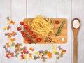 Dry Italian pasta fettuccini and farfalle with tomatoes, rosemary, mixture of peppers, spoon with flour and board