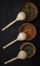 dry medicinal herbs in different containers with wooden spoons on a black wooden background