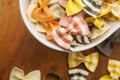 Dry multicolored Italian handmade macaroni called farfale, close-up in a white deep dish on a wooden background Royalty Free Stock Photo