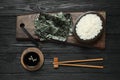 Dry nori sheets, rice, soy sauce and chopsticks on black wooden table, flat lay Royalty Free Stock Photo