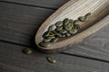 Dry organic styrian green pumpkin seeds on wooden plate over dark wooden background. Healthy food