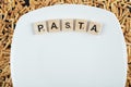 Dry pasta scattered around white plate with wooden letters