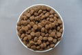 Dry pelleted pet food against a gray background. White ceramic bowl full of brown round pellets. Top view. Close-up