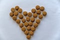 Dry pelleted pet food lined in a heart shape. Round brown pellets against a neutral background. Top view