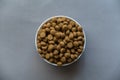 Dry pelleted pet food. White ceramic bowl full of round pellets. Gray background. Top view. Copy space