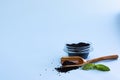 Dry raw sweet black basil seeds, other name tukhmaria or falooda or sabja in glass bowl and leaves blue background with