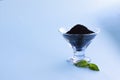 Dry raw sweet black basil seeds, other name tukhmaria or falooda or sabja in glass bowl and leaves blue background with