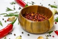 Dry red chili pepper slices in a round wooden bowl with peppercorns, garlic and rosemary on white food background. Royalty Free Stock Photo