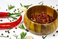Dry red chili pepper slices in a round wooden bowl with peppercorns, garlic and rosemary on white food background. Royalty Free Stock Photo