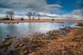 dry reeds on the shore and trees on a small lake, dramatic sky. Early spring, wide angle landscape Royalty Free Stock Photo