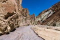 A dry riverbed of rocks and gravel curves through a canyon with colorful cliffs