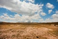 Dry soil under white clouds and blue sky. Mountains in perspective of sunny scene at high attitude