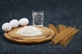 Dry spaghetti, flour on a cutting wooden board, chicken eggs and a glass of water Royalty Free Stock Photo