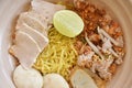 dry spicy tom yum Chinese yellow egg noodles with slice pork and ball couple fish line topping lemon on bowl