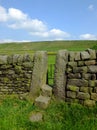 A dry stone wall with stone stile or narrow gate with steps in a yorkshire dales hillside meadow with a bright blue summer sky Royalty Free Stock Photo