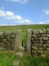 A dry stone wall with stone stile or narrow gate with steps in a yorkshire dales hillside meadow with a bright blue summer sky Royalty Free Stock Photo