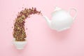 Dry tea pouring from teapot into cup on pink Royalty Free Stock Photo