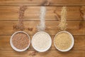 Dry uncooked rice in bowls on wooden table with piles of spilled grains, top view. Brown, red and white long basmati rice Royalty Free Stock Photo