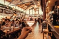 Dry wine in glass of hungry tourist inside crowd food market with fast-food stores and table for eating, Florence, Italy