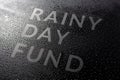 The dry words rainy day fund covered from water drops on black surface, unusual implementation concept