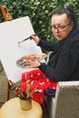 Old artist lady holding painter pallete and starting to paint on the empty canvas