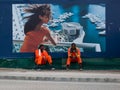 Dubai, UAE - March, 03 2017: Two construction workers resting in front of a luxury housing sign in the Dubai Marina area