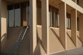 Corner of generic yellow office building with pillars, windows, and a ladder.