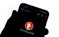 DuckDuckGo app on the smartphone screen hold by a silhouette of a hand. DuckDuckGo is an internet search engine focusing on user`