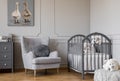 Ducks on cute oil painting in tasteful baby room with grey armchair and wooden crib, copy space on empty wall Royalty Free Stock Photo