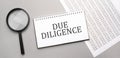 due diligence sign in white paper notepad and magnifying glass on the grey background Royalty Free Stock Photo