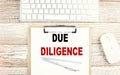 DUE DILIGENCE text on a clipboard with keyboard on wooden background