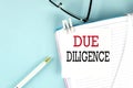 DUE DILIGENCE text on a sticky on notebook with pen and glasses , blue background