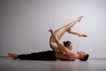 A duet of acrobats showing a pair trick. A woman in gymnastics overalls in a handstand over a shirtless man lies on his