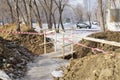 Dug trench with fence tape and wooden bridge above.