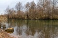 Dull cloudy autumn landscape, river bank and trees reflected in water Royalty Free Stock Photo