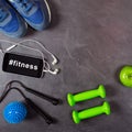 Dumbbell, apple, smartphone, headphones and sneakers on grey background. Hashtag fitness on the smartphone