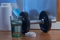 Dumbbell with a glass. Multivitamin and mineral pills, medical mask in the background.