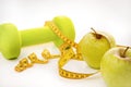 Dumbbell, green apples, yellow measuring tape on a white background